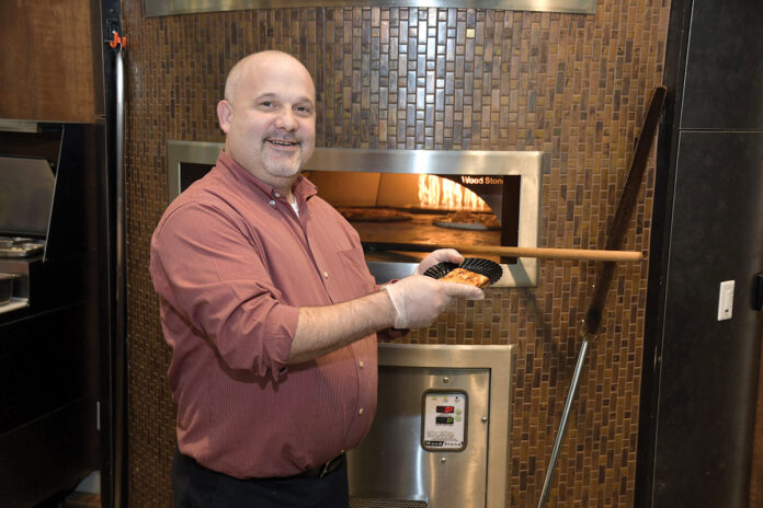 ADDED BENEFIT: Luis Melo, a chef in the campus cafeteria at the Citizens Bank headquarters complex in Johnston, takes pizza out of the oven. The oven is one of several amenities the bank has included at the campus to help retain current employees and recruit new ones. / PBN PHOTO/MIKE SKORSKI ADDED BENEFIT: Luis Melo, a chef in the campus cafeteria at the Citizens Bank headquarters complex in Johnston, takes pizza out of the oven. The oven is one of several amenities the bank has included at the campus to help retain current employees and recruit new ones. / PBN PHOTO/MIKE SKORSKI