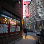 A PATRON walks near an entrance to a pizza restaurant, in Boston's North End neighborhood. Gov. Charlie Baker announced a $10 million small business recovery loan fund to help companies struggling because of efforts to slow the coronavirus pandemic. / AP FILE PHOTO/STEVEN SENNE