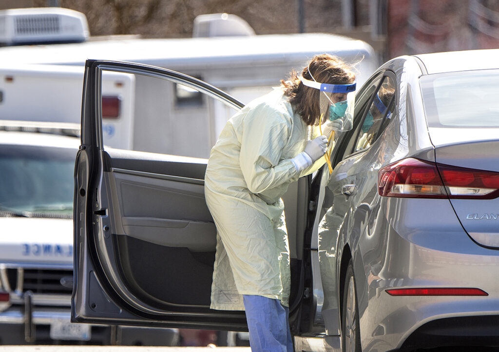 EARLY SCREENING: A health care worker at Kent County Memorial Hospital in Warwick conducts a preliminary examination at a patient’s car to determine if the patient needs a COVID-19 test or some other type of treatment. / PBN PHOTO/DAVE HANSEN