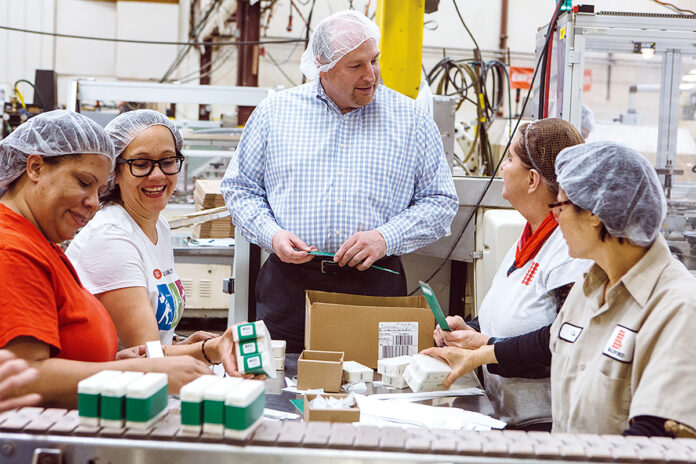 HELP WANTED: Bradford Soap Works Inc. in West Warwick is one of numerous Rhode Island companies hiring even though the economy has hit the skids during the corona­virus pandemic. In this 2018 file photo, CEO and President Stuart Benton works on the packing floor with Bradford employees. / PBN FILE PHOTO/RUPERT WHITELEY