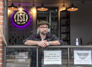 FREE SANITIZER: Liam Maloney, tasting room manager at The Industrious Spirit Co. in Providence, stands at the company&rsquo;s &ldquo;drive-up&rdquo; window, where it is offering people free bottles of hand sanitizer that it makes using the byproduct of its vodka manufacturing. / PBN PHOTO/MICHAEL SALERNO