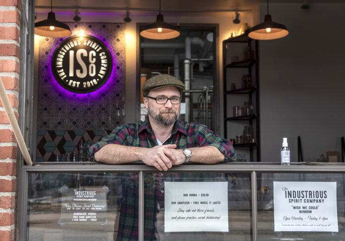 FREE SANITIZER: Liam Maloney, tasting room manager at The Industrious Spirit Co. in Providence, stands at the company’s “drive-up” window, where it is offering people free bottles of hand sanitizer that it makes using the byproduct of its vodka manufacturing. / PBN PHOTO/MICHAEL SALERNO FREE SANITIZER: Liam Maloney, tasting room manager at The Industrious Spirit Co. in Providence, stands at the company’s “drive-up” window, where it is offering people free bottles of hand sanitizer that it makes using the byproduct of its vodka manufacturing. / PBN PHOTO/MICHAEL SALERNO