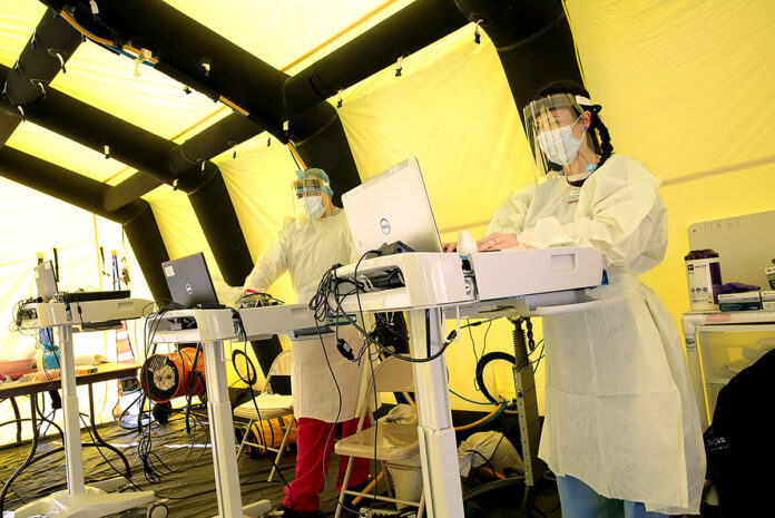 PREPARED: Health workers type on laptops inside the incoming COVID-19 patient tent set up outside the Emergency Department at Rhode Island Hospital in ­Providence.  COURTESY LIFESPAN CORP.