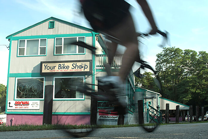 STAYING SAFE: A new PBN survey found many Rhode Islanders won’t feel safe around large groups of people until next year. For businesses that rely on tourism, that might mean a renewed focus on family activities this summer, including bike tours. Above, a cyclist passes Your Bike Shop in Warren. / PBN FILE PHOTO/RYAN T. CONATY