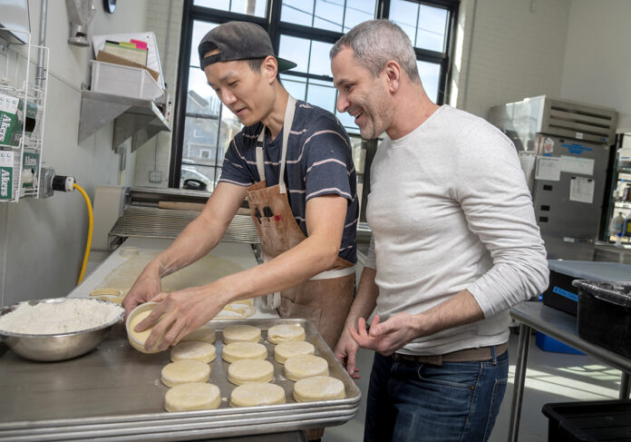 WEEKEND WARRIORS: Knead Doughnuts co-owner Adam Lastrina, right, and Bryan Tsai, production supervisor, prepare doughnuts in March. While the bakery has three locations in Rhode Island, only one remains open, serving takeout orders on the weekends only. / PBN FILE PHOTO/MICHAEL SALERNO WEEKEND WARRIORS: Knead Doughnuts co-owner Adam Lastrina, right, and Bryan Tsai, production supervisor, prepare doughnuts in March. While the bakery has three locations in Rhode Island, only one remains open, serving takeout orders on the weekends only. / PBN FILE PHOTO/MICHAEL SALERNO