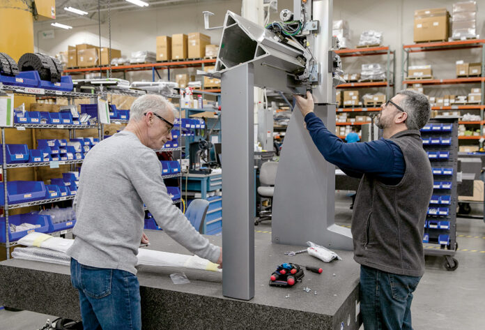 ENVIRONMENTALLY FRIENDLY: Hexagon Manufacturing Intelligence has implemented multiple initiatives to limit impacts on energy and resources. From left, Thomas Conway, assembly technician, and David Auclair, global department lead, work on a machine at the North Kingstown facility. / PBN PHOTO/TRACY JENKINS ENVIRONMENTALLY FRIENDLY: Hexagon Manufacturing Intelligence has implemented multiple initiatives to limit impacts on energy and resources. From left, Thomas Conway, assembly technician, and David Auclair, global department lead, work on a machine at the North Kingstown facility. / PBN PHOTO/TRACY JENKINS
