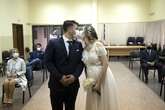GOING THROUGH WITH IT: Groom Raul Benitez and bride Jenny Bonet wear protective face masks as they kiss during their wedding ceremony at the Civil Registry office, in Asuncion, Paraguay, in June.  / AP FILE PHOTO/JORGE SAENZ