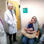 TEAM EFFORT: Lifespan’s Dr. Francois Luks, left, and Care New England’s Dr. Stephen Carr meet in 2018 with parents Emily and Brian Hess, of Attleboro, as Emily holds her infant son, Selwyn. The doctors had operated on Selwyn in utero as part of the Fetal Treatment Program, a collaborative initiative of CNE and Lifespan. The boy at right is another one of the Hess’ children. / COURTESY LIFESPAN CORP.