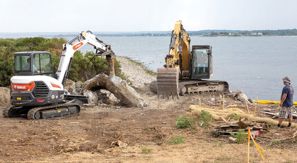 AT THE CONTROLS: Aquidneck Landworks Inc. workers Bryan Clooney, in white excavator, and Joel Camara, in yellow excavator, demolish and excavate a patio near the shore of the Sakonnet River in Portsmouth. The Back to Work RI program may be an opportunity for the landscape company to find qualified workers, as owner Rick Miranda says he’s been hard-pressed to do so amid the industry’s growth in recent years. / PBN PHOTO/KATE WHITNEY LUCEY