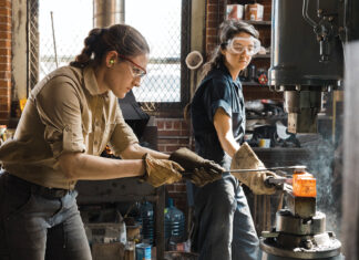 HEATING UP: Alaina Mahoney, left, of Providence-based A.M. Design & Fabrication LLC, works with assistant Erica Compton heating metal in a forge to hammer out a mirror frame for Mahoney’s upcoming product line release.  / COURTESY RUE SAKAYAMA PHOTOGRAPHY