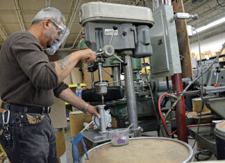 PUMPING OUT PRODUCT: The Bosworth Co.’s machine shop supervisor, who asked not to be named, uses a drill press to tap holes into the aluminum body of the Guzzler diaphragm pump. CEO and President Douglas Reilly, not pictured, said the East Providence pump manufacturer saw an increased demand for the Guzzler, a small, foot-operated pump used in portable sinks and hand-wash stations, during the coronavirus pandemic. / PBN PHOTO/ELIZABETH GRAHAM 