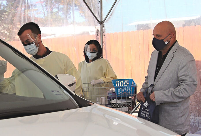 HEALTHY DISTRIBUTION: Joseph DeSantis, right, CEO and president of Tri-County Community Action Agency, and Jacquelyn Lorenti, medical assistant, help distribute COVID-19 kits at the agency’s testing site in Johnston, while Medical Director Dr. Wilfredo Giordano-Perez, left, administers a COVID-19 test. The kits distributed by the group include masks, sanitizing wipes, hand sanitizer, tissues and health-related educational information. / COURTESY TRI-COUNTY COMMUNITY ACTION AGENCY