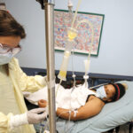 CLOSE WATCH: Registered nurse Jessica Pace, left, who works in the Rhode Island Hospital and Hasbro Children’s Hospital Emergency Department, checks the intravenous line of Dolce Contreras, 32, of Central Falls, who is receiving convalescent plasma therapy as part of a clinical trial on its effectiveness against COVID-19. / COURTESY LIFESPAN CORP./WILLIAM MURPHY