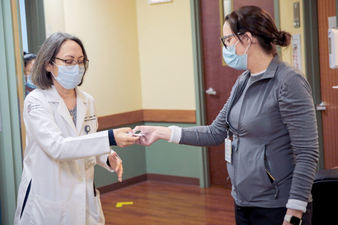 IN GOOD HANDS: Jennifer Beaugh, right, pharmacy supervisor at The Miriam Hospital, hands a dose of COVID-19 vaccine to Dr. Karen Tashima at a clinic at The Miriam. Tashima is overseeing a clinical trial of the COVID-19 vaccine that hasn’t yet received U.S. government approval. / COURTESY LIFESPAN CORP. IN GOOD HANDS: Jennifer Beaugh, right, pharmacy supervisor at The Miriam Hospital, hands a dose of COVID-19 vaccine to Dr. Karen Tashima at a clinic at The Miriam. Tashima is overseeing a clinical trial of the COVID-19 vaccine that hasn’t yet received U.S. government approval. / COURTESY LIFESPAN CORP.