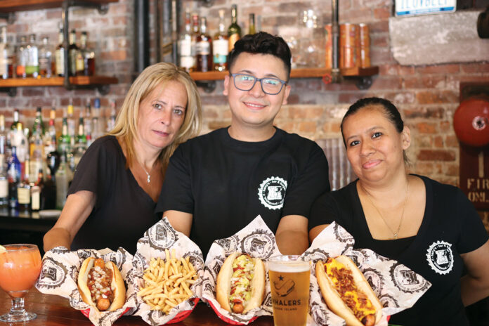 THE WORKS: From left, Harry’s Bar & Burger staff members Lynn Perrino, Kelvin Agustin and Sonia Real display Gastros Craft Meats hot dogs at the restaurant’s Atwells Avenue location in Providence. The comfort food is on the Harry’s menu at all locations. / COURTESY CHRISTINA MONAHAN
