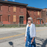 REBIRTH? Jan Brodie, executive director of the Pawtucket Foundation, stands outside an abandoned industrial building at Conant and Pine streets in Pawtucket that city officials hope will be part of the redevelopment envisioned around a commuter rail and bus station scheduled to be finished in 2022. / PBN PHOTO/MICHAEL SALERNO
