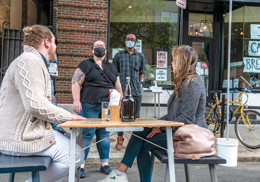 READY AND WAITING: Servers Makayla Habershaw, standing left, and Ahmed Sesay take the food orders of Jeffrey Bibeau, sitting left, of Providence and Riley Farrar of Washington, D.C., at a sidewalk table at north on Fountain Street in Providence. / PBN PHOTO/MICHAEL SALERNO