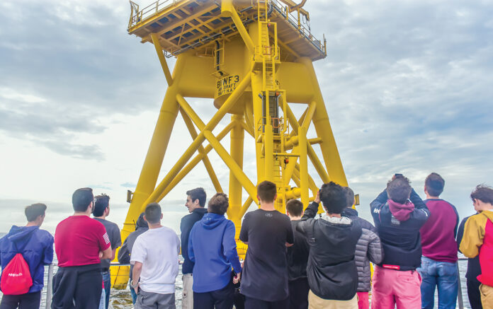 FUTURE WORKFORCE? Rhode Island high school students participating in a career pathway program for offshore wind jobs ride in a boat circling a Block Island Wind Farm turbine. / COURTESY DOUG LEARNED/LUCKY DAWG PHOTOGRAPHY
