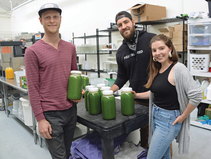 MAJOR GROWTH: From left, juicing company Fully Rooted Inc. co-owners Benjamin Aalvik, Angelo Mollis and Amanda Repose in their production space in Pawtucket. Although the retail store had to close and farmers market sales were cut in half during the COVID-19 pandemic, delivery across Rhode Island and Massachusetts grew exponentially. / PBN PHOTO/ELIZABETH GRAHAM MAJOR GROWTH: From left, juicing company Fully Rooted Inc. co-owners Benjamin Aalvik, Angelo Mollis and Amanda Repose in their production space in Pawtucket. Although the retail store had to close and farmers market sales were cut in half during the COVID-19 pandemic, delivery across Rhode Island and Massachusetts grew exponentially. / PBN PHOTO/ELIZABETH GRAHAM