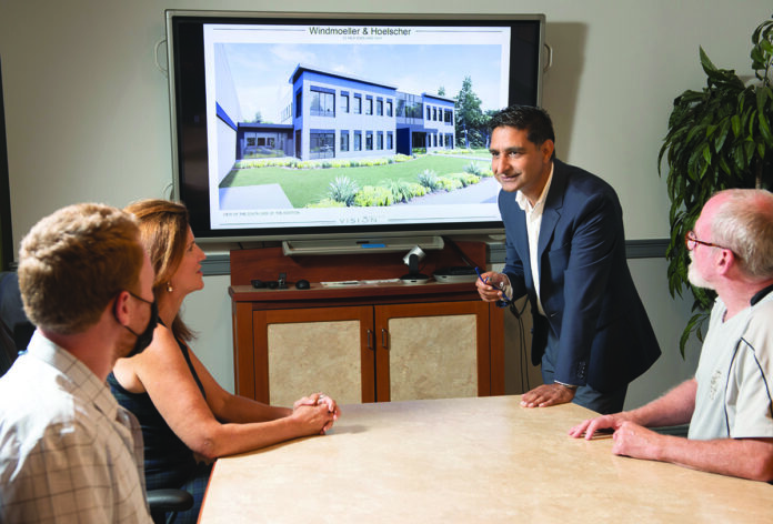 SNEAK PEEK: Windmoeller & Hoelscher Corp. Senior Vice President Javeed Buch, standing, meets with staffers at the firm’s North American headquarters in Lincoln. On the screen is an artist’s rendering of the company’s future offices that are soon to be under construction. / PBN PHOTO/DAVE HANSEN SNEAK PEEK: Windmoeller & Hoelscher Corp. Senior Vice President Javeed Buch, standing, meets with staffers at the firm’s North American headquarters in Lincoln. On the screen is an artist’s rendering of the company’s future offices that are soon to be under construction. / PBN PHOTO/DAVE HANSEN