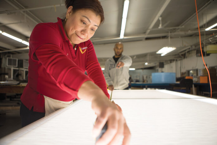 BRILLIANT JOB: Lumetta Inc. employees Mirna DeLaCruz, in the foreground, and Yonfi Polanco work at a light table in the manufacturer’s facilities in Warwick.  / COURTESY LUMETTA INC.