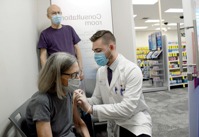 EARLY PROTECTION: Mary Norwalk gets her flu shot from Matt Lefebvre, pharmacy manager at the CVS store on Hope Street in Providence, while Art Norwalk, Mary’s husband, looks on. / PBN PHOTO/ELIZABETH GRAHAM
