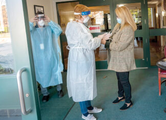 A time of upheaval and recovery TAKING NO CHANCES: In November 2020, Elizabeth “Libby” Sarro, right, administrator at Bethany Home of Rhode Island, helps office manager Linda Wilson, center, and David Bragga, director of therapy, don protective equipment at the entrance of the Providence nursing home. / PBN FILE PHOTO/MICHAEL SALERNO