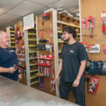 NEXT GEN: M&G Plumbing Supply Co. owner Richard Correia, left, speaks with stock clerk Alex Knowles. Correia is of Portuguese descent but sees no need to participate in the state Minority Business Enterprise program. His father, John, emigrated from the Azores and started in the business in the 1960s. / PBN PHOTO/MICHAEL SALERNO