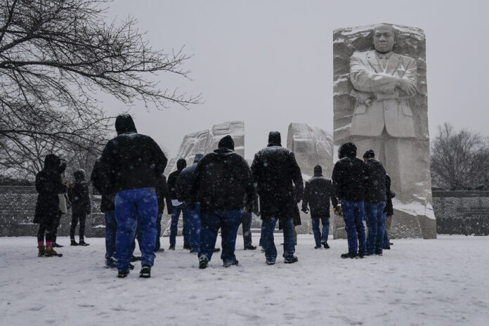 VISITORS APPROACH the Martin Luther King Jr. Memorial in Washington, D.C., as snow falls on Sunday. Ceremonies scheduled at the site on Monday to mark the national holiday were canceled because of the weather. AP PHOTO/CAROLYN KASTER