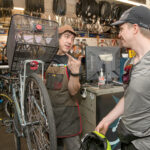 ON THE RISE: James Sawyer, left, shop manager of Legend Bicycle LLC in Providence, assists Nick Seidler. Sawyer says he could see bike-specific insurance policies become more popular as demand for electric bikes increases. / PBN PHOTO/MICHAEL SALERNO