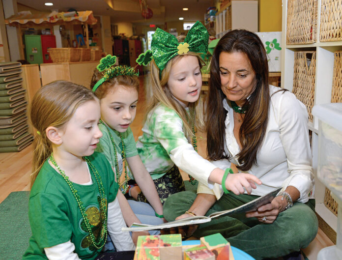 QUALITY TIME: Heather Mayo, founder and owner of Sweet Peas Village in East Greenwich, reads to a few kindergarten students on St. Patrick’s Day. The school has 22 classrooms and serves 230 students between the ages of 6 weeks and 5 years old. / PBN PHOTO/ELIZABETH GRAHAM