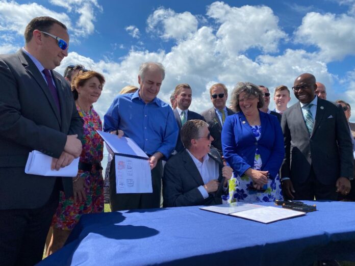 GOV. DANIEL J. MCKEE (center) signed legislation into law on Wednesday requiring the state's primary utility company to buy up to 1,000 megawatts of offshore wind power. /COURTESY OFFICE OF GOV. DANIEL J. MCKEE