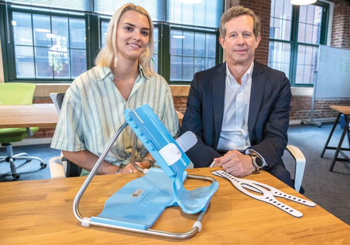 BABY STEPS: Maey Petrie, left, director of programs and business developent at New England Medical Innovation Center, and Robert Cooper, SmölTap CEO, with the product designed to hold infants still while undergoing a spinal tap. It will launch this fall.  PBN PHOTO/MICHAEL SALERNO