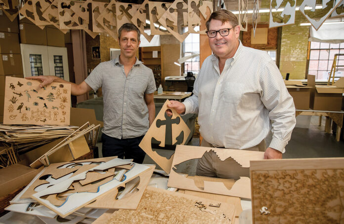 RHODY PUZZLES: Sam White, left, lead designer, and Jerauld Adams, owner, make puzzles with unique, Rhode Island-inspired designs at their Pawtucket manufacturing company Hope Puzzles LLC. PBN PHOTO/TRACY JENKINS