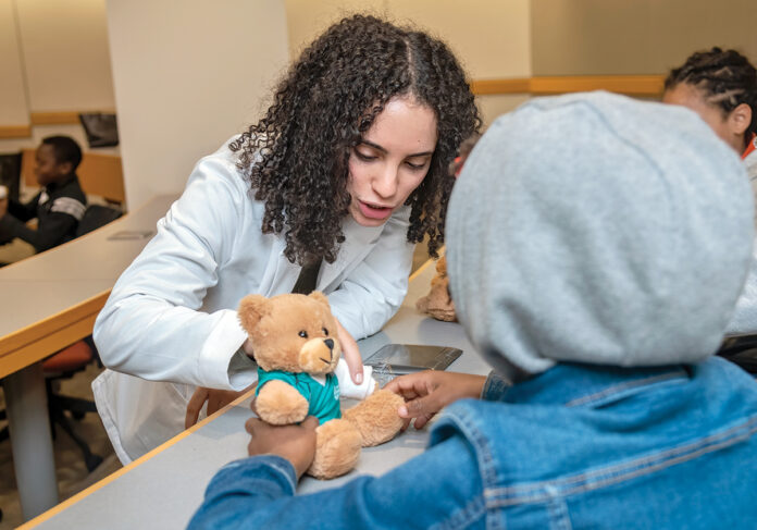 ON THE MEND: Anna Rezk, a Warren Alpert Medical School student, checks the casting work of a youngster who was assigned to treat a teddy bear with a broken arm at the Black Men in White Coats youth summit at the Brown University medical school in October.  PBN PHOTO/MICHAEL SALERNO