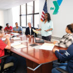 UNITED: YMCA of Greater Providence Assistant Director of Diversity, Equity and Inclusion Kira Wills, standing, addresses her colleagues at the organization’s Providence office. Wills says the YMCA is for all, which is reflected by its staff being comprised of individuals who are neurodivergent, have disabilities, speak multiple languages, identify as LGBTQIA and are different ages. PBN PHOTO/DAVID HANSEN