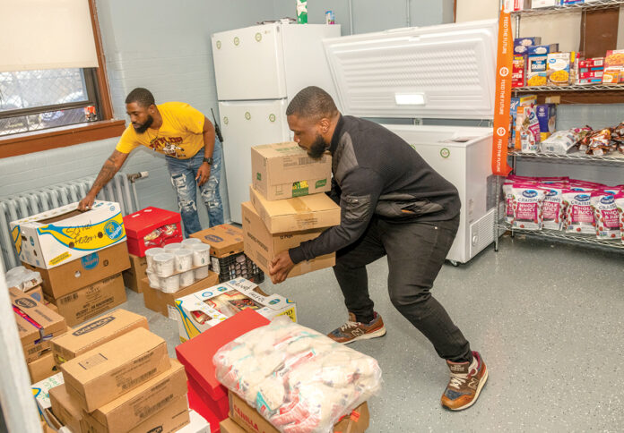 DELIVERING THE GOODS: Dustin Ford, left, community specialist in the Providence school system in charge of the Mount Pleasant High School food pantry, and John Nagbe, community outreach manager at We Share Hope, deliver donations to the high school’s recently opened food pantry, which provides students with food during holiday breaks, nights and weekends. PBN PHOTO/MICHAEL SALERNO