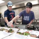 REACHING OUT: LaSalle Academy students JJ Sanzi, left, and Cole ­Matthews volunteer by preparing meals at the Amos House food kitchen in Providence. PBN PHOTO/MICHAEL SALERNO