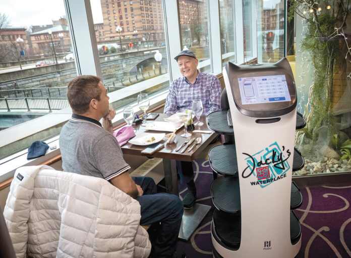 ROLLING OUT: Jacky’s Waterplace Sushi Bar robot server “Bella” waits on a table with Ignacio Davila, left, and Galen Tate. PBN PHOTO/­MICHAEL SALERNO