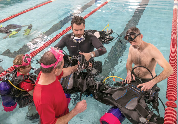 SCUBA SESSION: Brady Watson, center background, dive master with Dive On It Scuba, teaches members of Boy Scout  Troop 44 of Walpole, Mass., in the pool at Cumberland High School. From left are Danny Federer; his father, Chris Federer; and Mike Ahlfont. PBN PHOTO/MICHAEL SALERNO