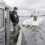 NAVIGATING SHORTAGES:  R.I. environmental police officer Jacob Malone, left, checks the size of striped bass caught by two unidentified fishermen in Narragansett Bay. The R.I. Department of Environmental Management says staff shortages have made it difficult to schedule such law enforcement ­operations.  PBN PHOTO/ DAVID HANSEN