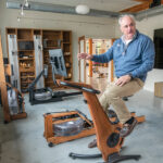 BLENDING IN: WaterRower Inc. CEO and President Peter King demonstrates one of the company’s stationary bikes in its showroom in Warren. King says the aesthetics of the equipment, which resembles furniture, is one of its most functional elements. PBN PHOTO/MICHAEL SALERNO