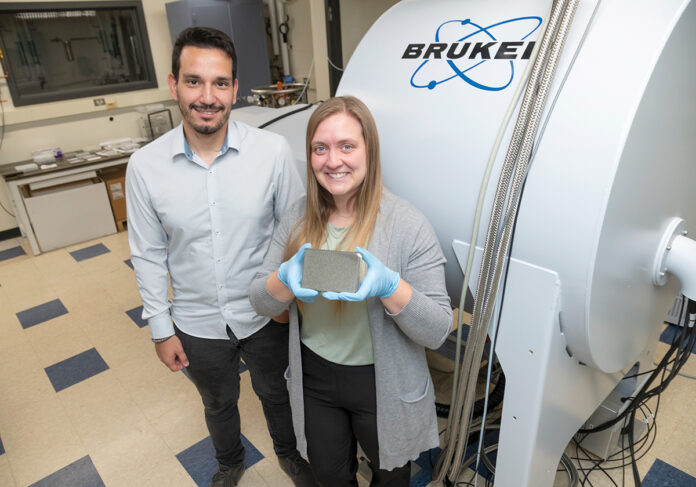 ON THE EDGE: Selahaddin Gumus, left, and Dana Biechele-Speziale are co-founders of deep-tech startup AtomICs Inc., which is developing molecular-level data storage that allows more information to be stored in a smaller amount of space, more sustainably and for longer periods of time. Biechele-Speziale is holding an aluminum plate that inserts into and is read by the mass spectrometer behind them.  PBN PHOTO/MICHAEL SALERNO