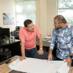 PLANNING AHEAD: James Hernandez, left, E2SOL LLC’s lead electrician, and Brandon Baro, field site support specialist, look over design plans at the renewable energy firm’s Providence office.  PBN PHOTO/TRACY JENKINS