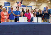 SIGNED ON THE LINE: Newport Mayor Xaykham “Xay” Khamsyvoravong, seated at right, ceremonially agrees in April to participate in Gov. Daniel J. McKee’s Learn365RI out-of-school learning initiative. McKee is sitting at left. R.I. Education Commissioner Angélica Infante-Green stands between McKee and Khamsyvoravong. The signing took place at the Boys & Girls Clubs of Newport County.  COURTESY GOV. DANIEL J. MCKEE’S OFFICE
