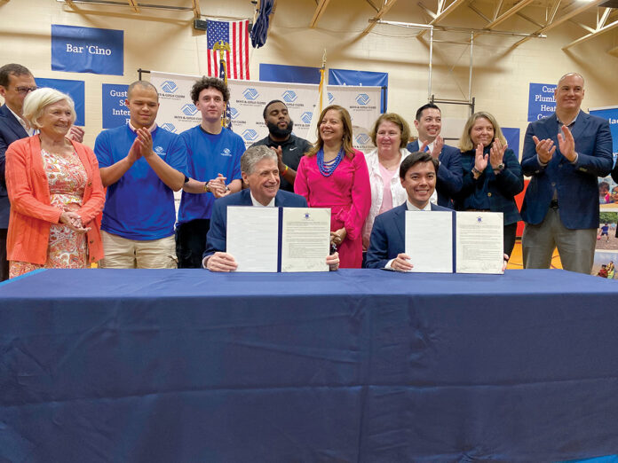 SIGNED ON THE LINE: Newport Mayor Xaykham “Xay” Khamsyvoravong, seated at right, ceremonially agrees in April to participate in Gov. Daniel J. McKee’s Learn365RI out-of-school learning initiative. McKee is sitting at left. R.I. Education Commissioner Angélica Infante-Green stands between McKee and Khamsyvoravong. The signing took place at the Boys & Girls Clubs of Newport County.  COURTESY GOV. DANIEL J. MCKEE’S OFFICE