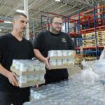HEAVY LIFTING: Joe Parillo, left, warehouse expeditor, and Joe Regan, warehouse manager, unload cases of canned goods at the Rhode Island Community Food Bank’s distribution center in Providence. PBN PHOTO/ELIZABETH GRAHAM