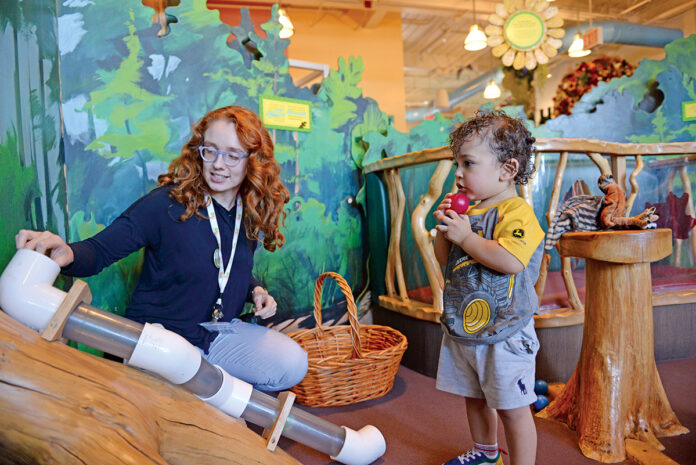 PLAYTIME: Jordan Towle, a visitor services manager at the Providence Children’s Museum, plays with Jorge Rodrigues, 1, of Providence. The museum, according to Executive Director Caroline Payson, relies on ticket sales and membership fees to bolster operating costs.  PBN PHOTO/ELIZABETH GRAHAM