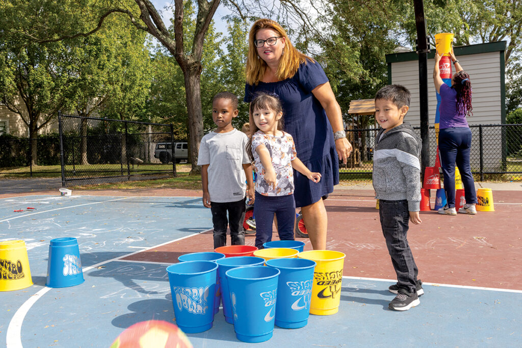 BUCKET BRIGADE: Dr. Martin Luther King Jr. ­Community Center ­Executive Director Heather Hole Strout, center, plays a bucket game with  a group of preschoolers  at the Newport-based  nonprofit’s playground.  PBN PHOTO/KATE WHITNEY LUCEY
