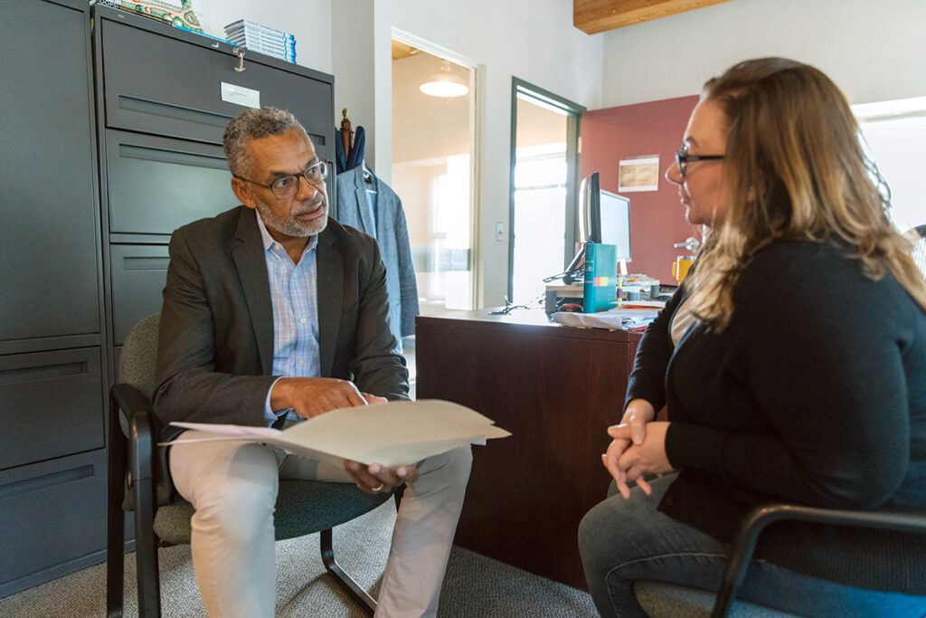 A PRESENT NEED: The Groden ­Network CEO ­Michael Pearis, left, speaks with ­Marketing ­Coordinator Hope Cahill in his office. Pearis says there is a 15% employee vacancy rate  at the ­Providence-based social services ­organization, ­leading to more overtime costs.  PBN PHOTO/RUPERT WHITELEY